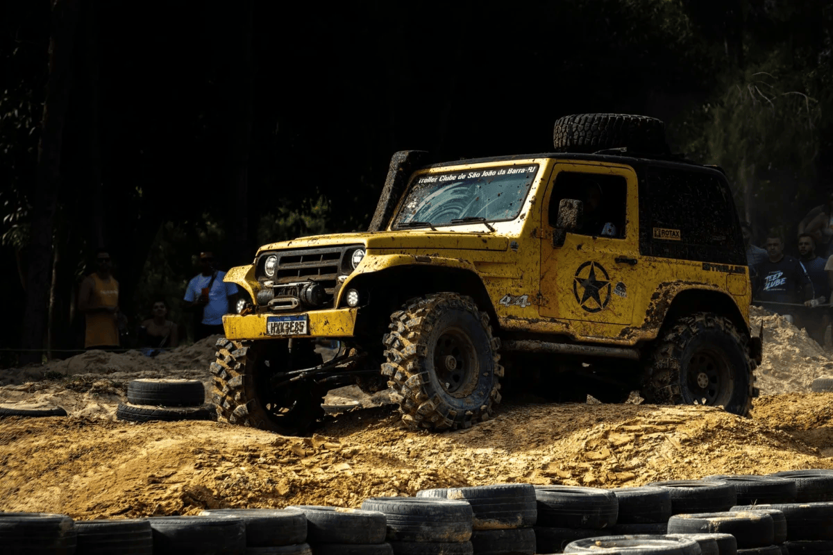 Yellow off-road vehicle navigating through a rugged, muddy terrain during an outdoor challenge event.