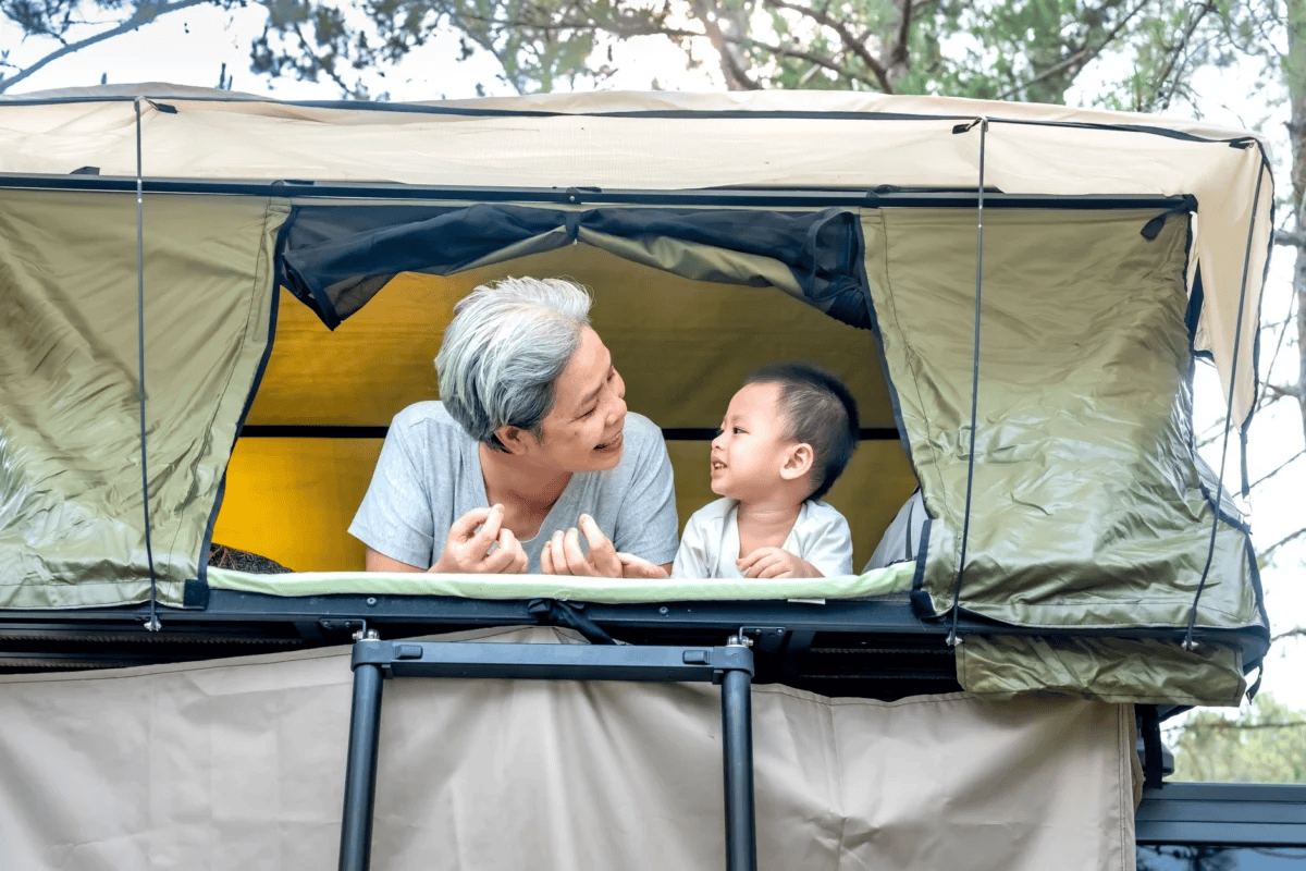 A senior and child enjoying outdoor rooftop tent camping, sharing smiles.