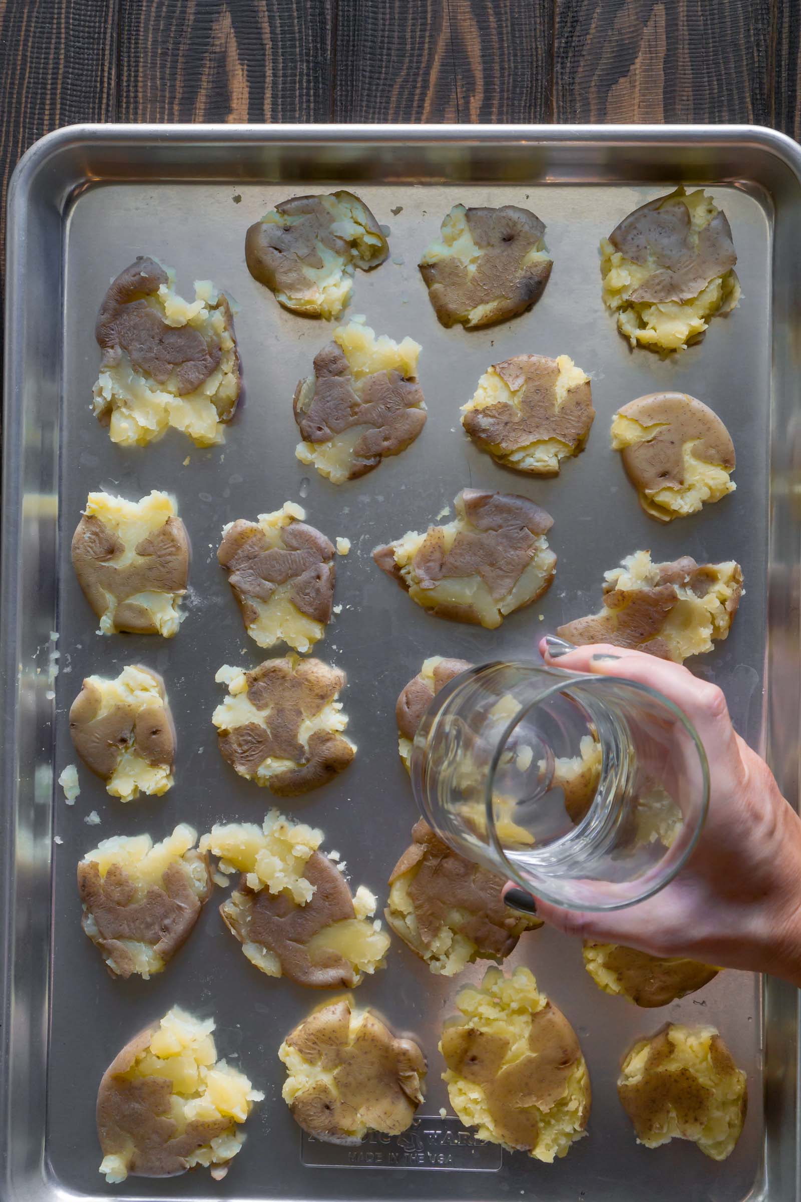a glass smashing potatoes on a baking sheet