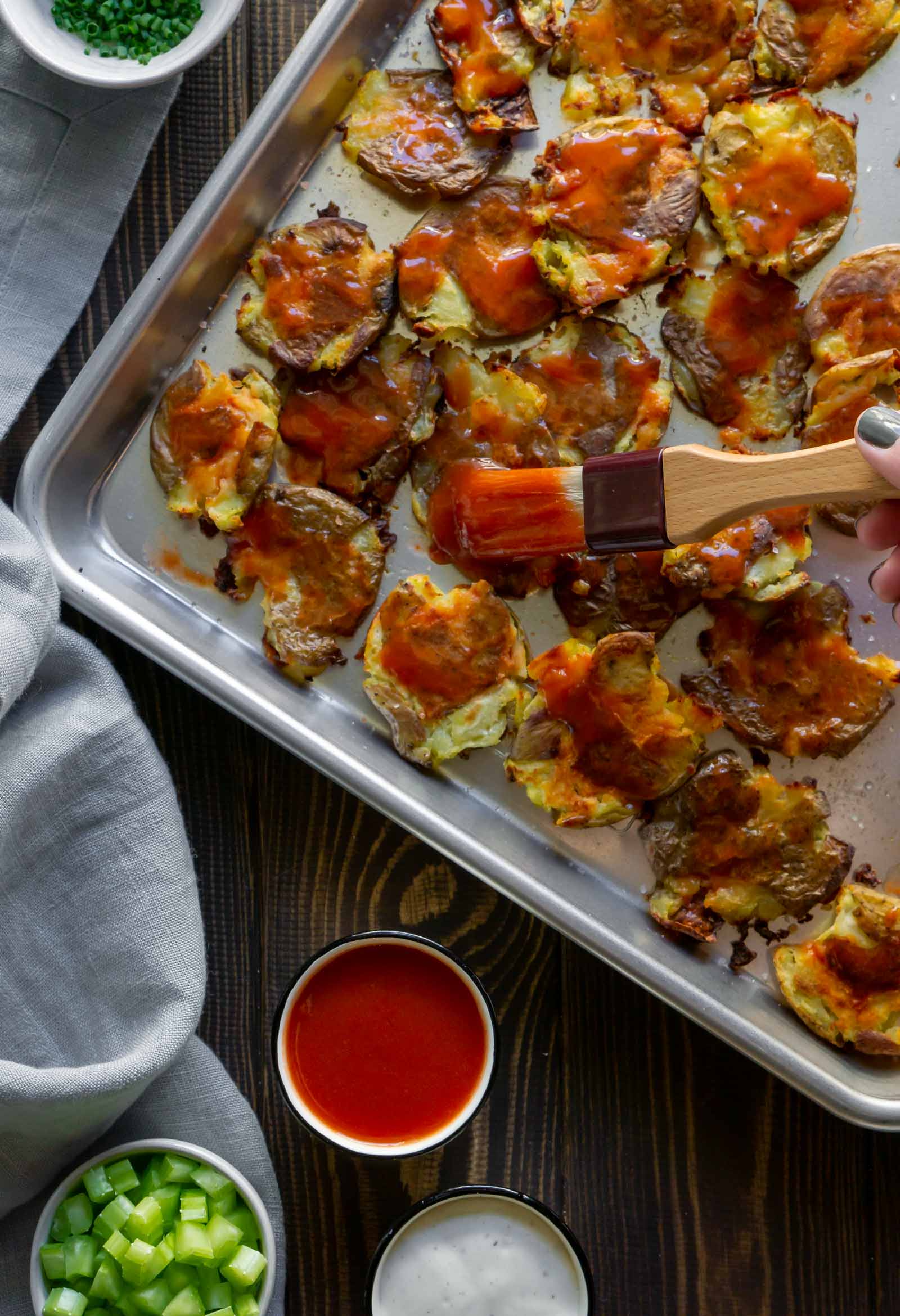 a pastry brush covering smashed potatoes with bbq sauce