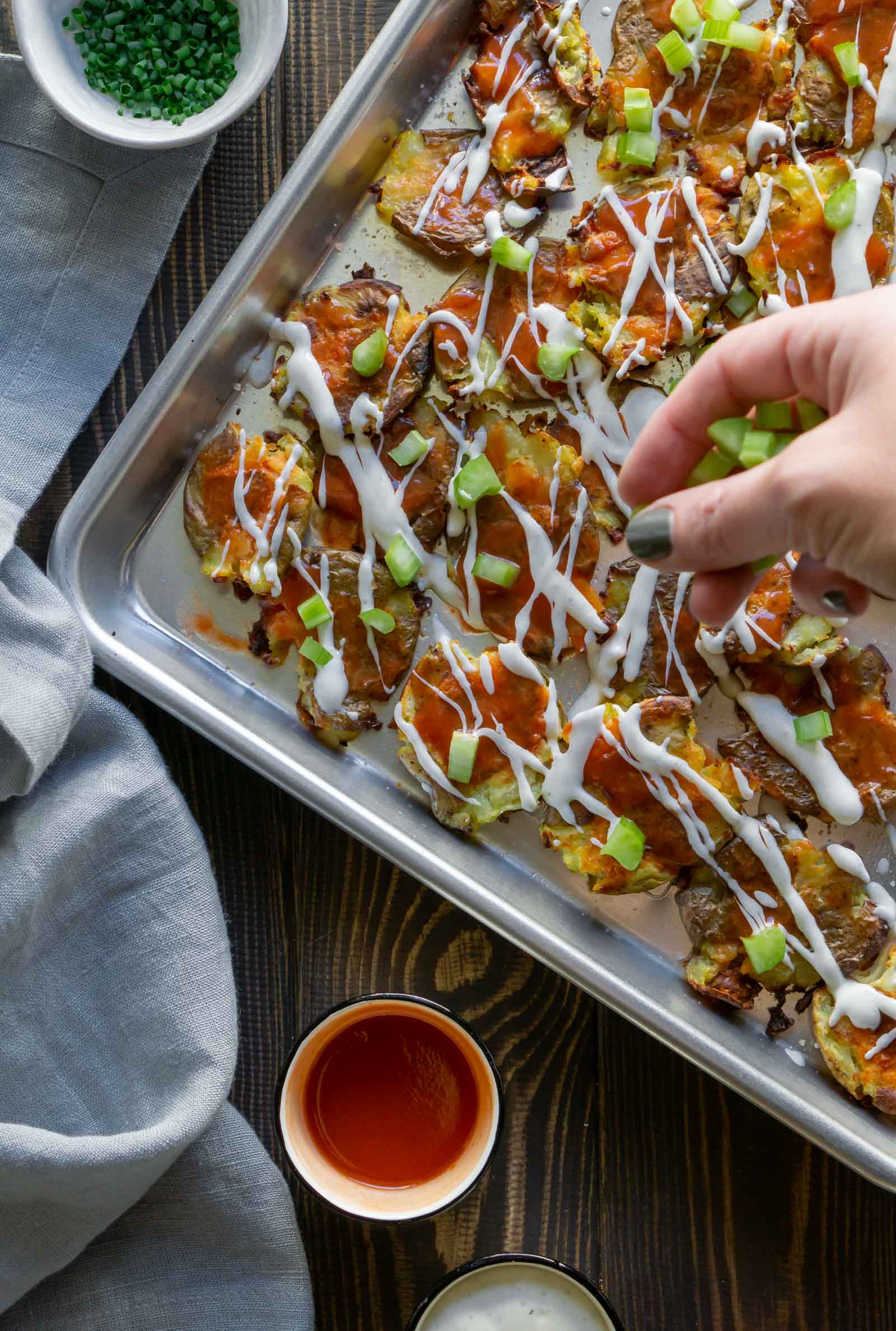 a hand sprinkling celery over the smashed potatoes
