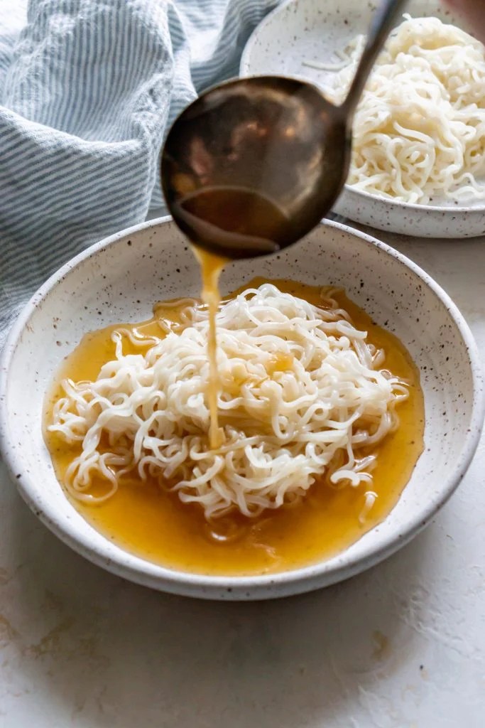 ladle pouring broth over rice noodles