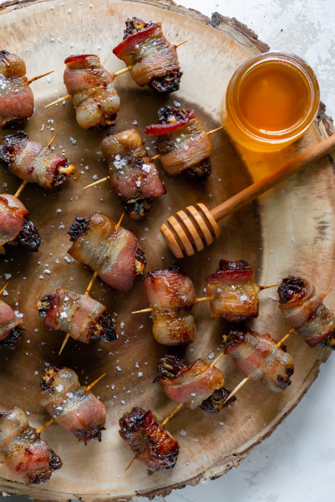 bacon wrapped dates on a wood serving tray with honey