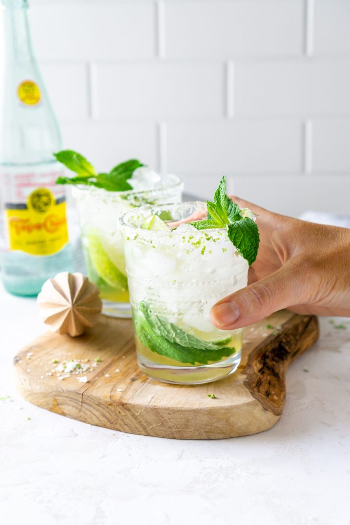 hand holding a mojito on a wood serving tray