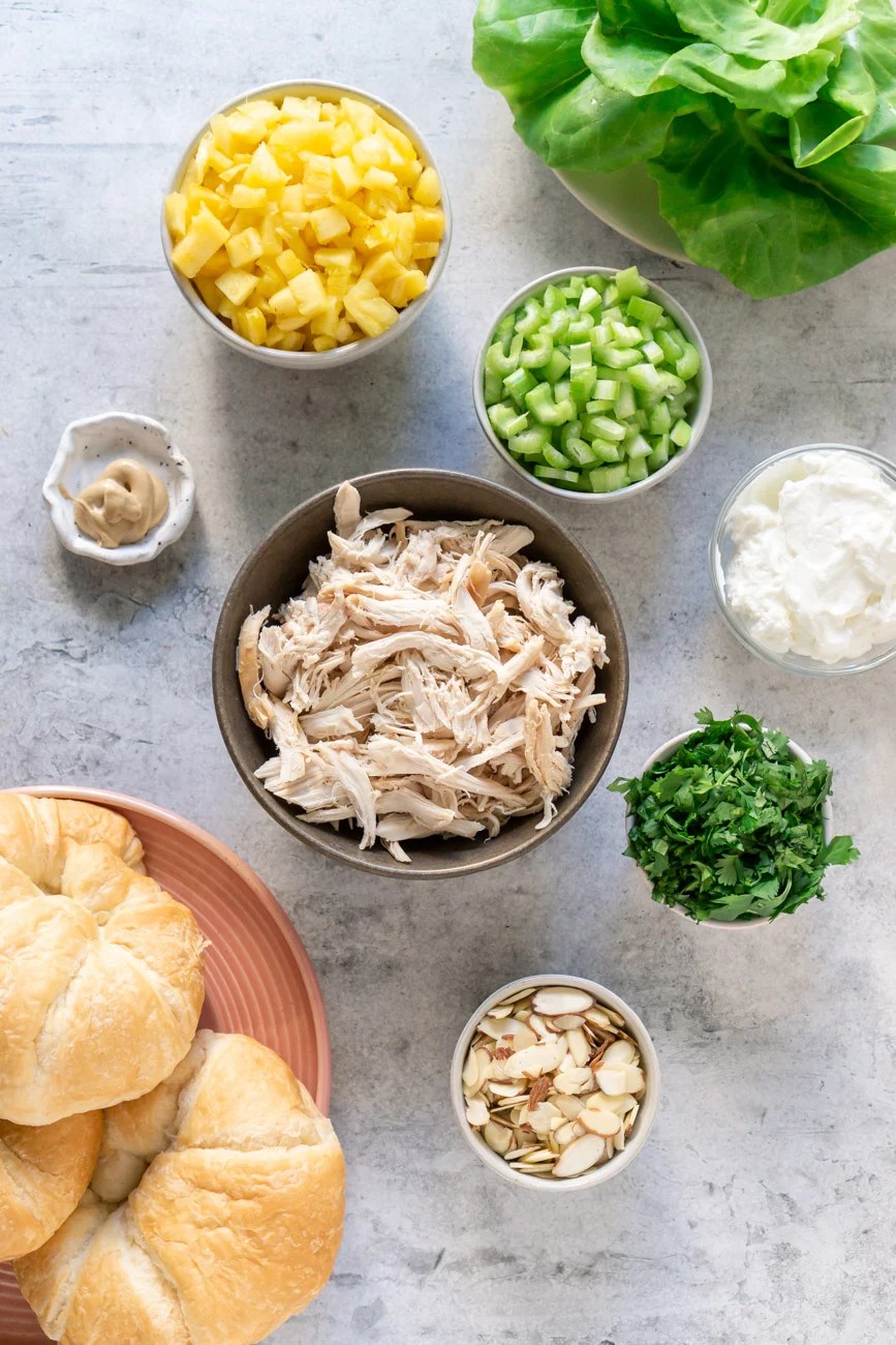 ingredients in small bowls - chicken, mango, celery, cilantro, almonds, lettuce, croissants