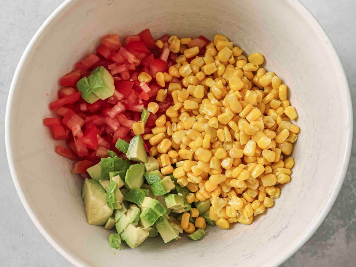 A bowl with diced tomatoes, corn and avocado ready to combine with the other corn salsa ingredients. 