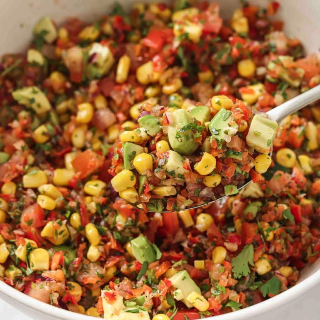 A spoon holding a scoop of corn salsa with avocado showing the various textures and ingredients. 