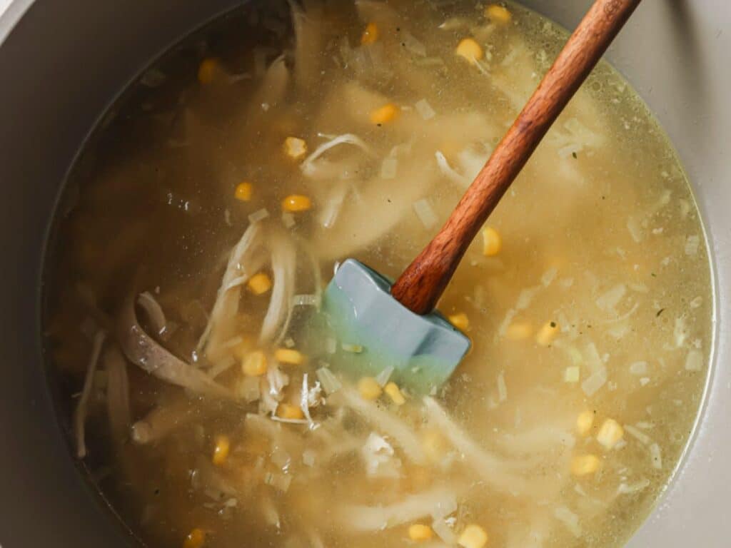 Chicken stock, shredded chicken, and corn added to the pot before simmering.