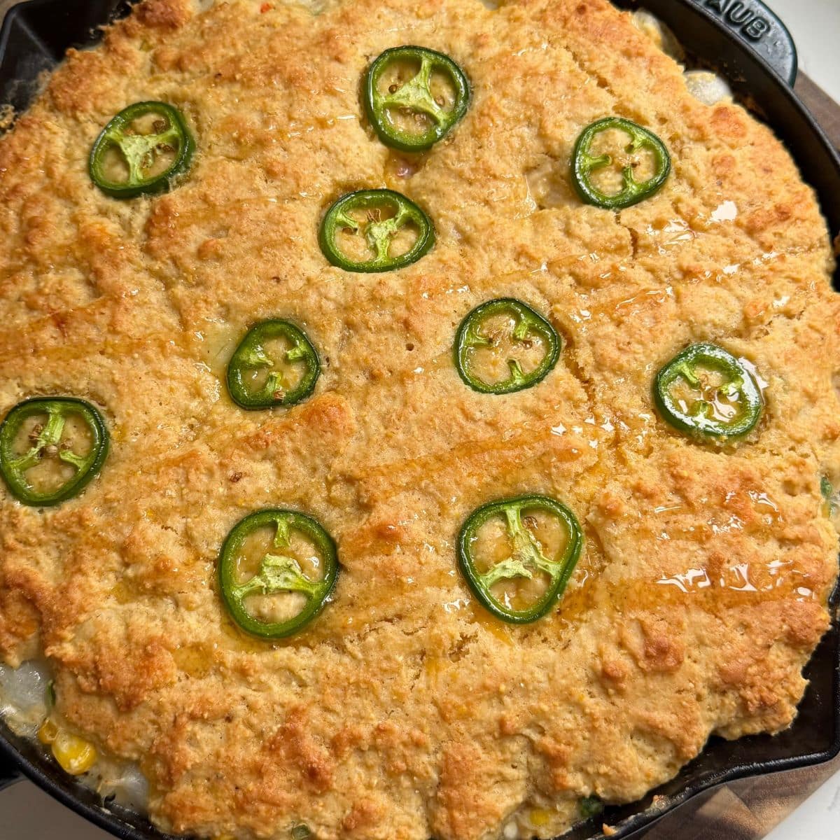 Close-up of a cornbread pot pie topped with cheddar cornbread and sliced jalapeños.