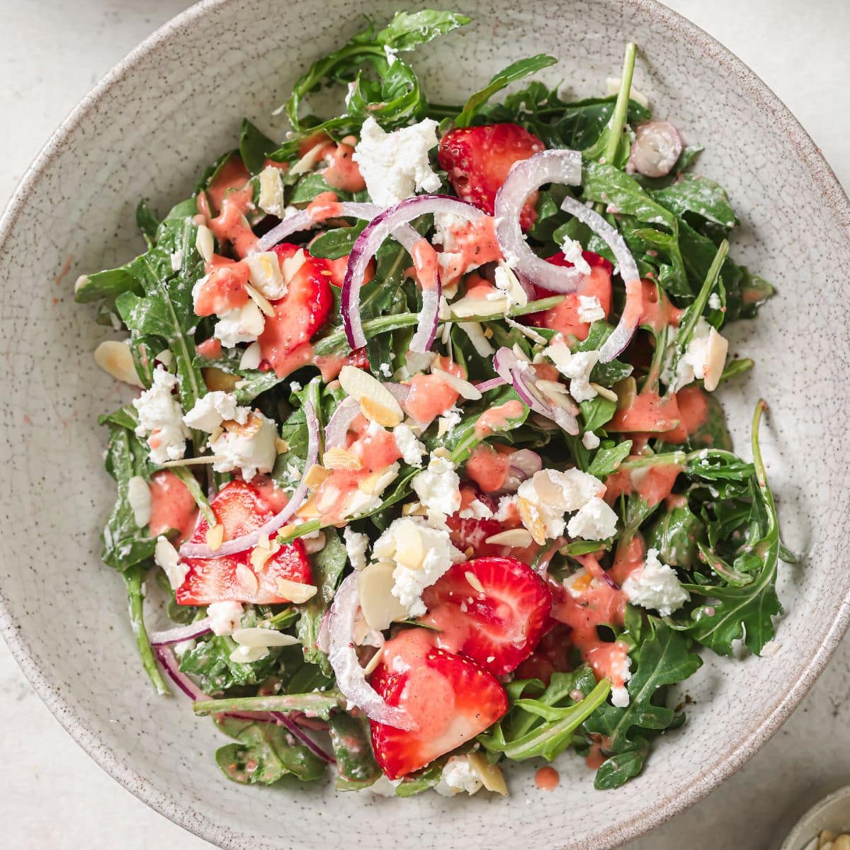 Strawberry arugula salad in a bowl with red onions, fresh strawberries, goat cheese, all tossed in a fresh strawberry vinaigrette.