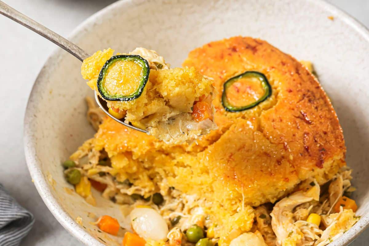 A slice of cornbread chicken pot pie on a white dish with a fork scooping out a bite.