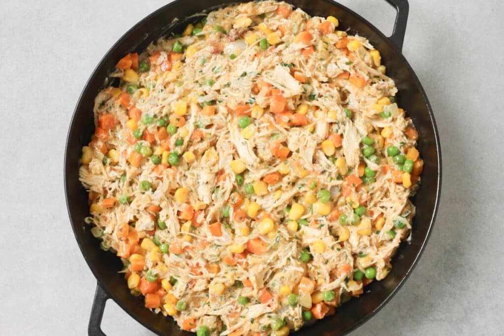 Placing the pot pie filling mixture into a pie dish before topping with cornbread.
