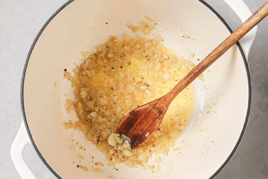 Sauteeing aromatics in a pan with oil, a wooden spoon resting on the side.