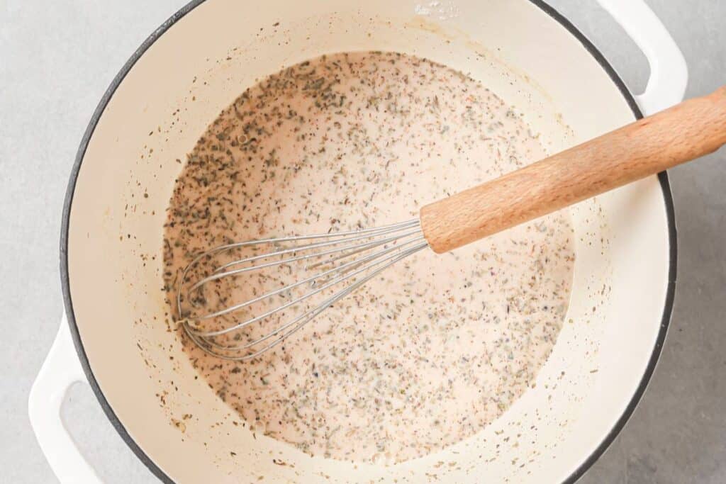 Whisking chicken stock and milk into the roux to make the base of the chicken pot pie filling.