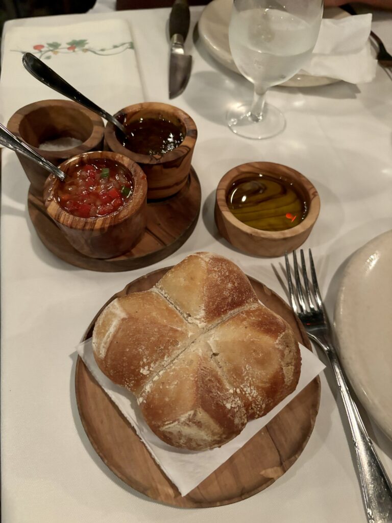 Before looking at the menu at Parrilla Don Julio Buenos Aires: Bread shaped like a flower with salsas and olive oil. Plates displayed on a white tablecloth.