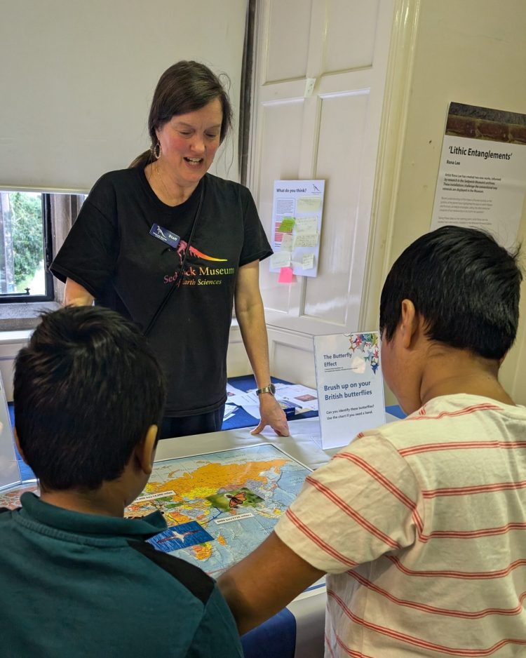 A member of staff from the Sedgwick Museum of Earth Sciences engaging with two children. They are all interacting with a world map.