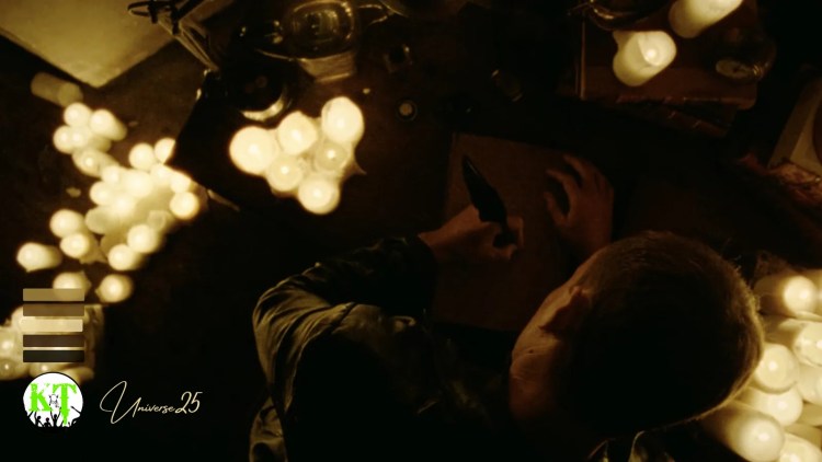 The Angel from the film Universe25 at his desk, writing, surrounded by candles