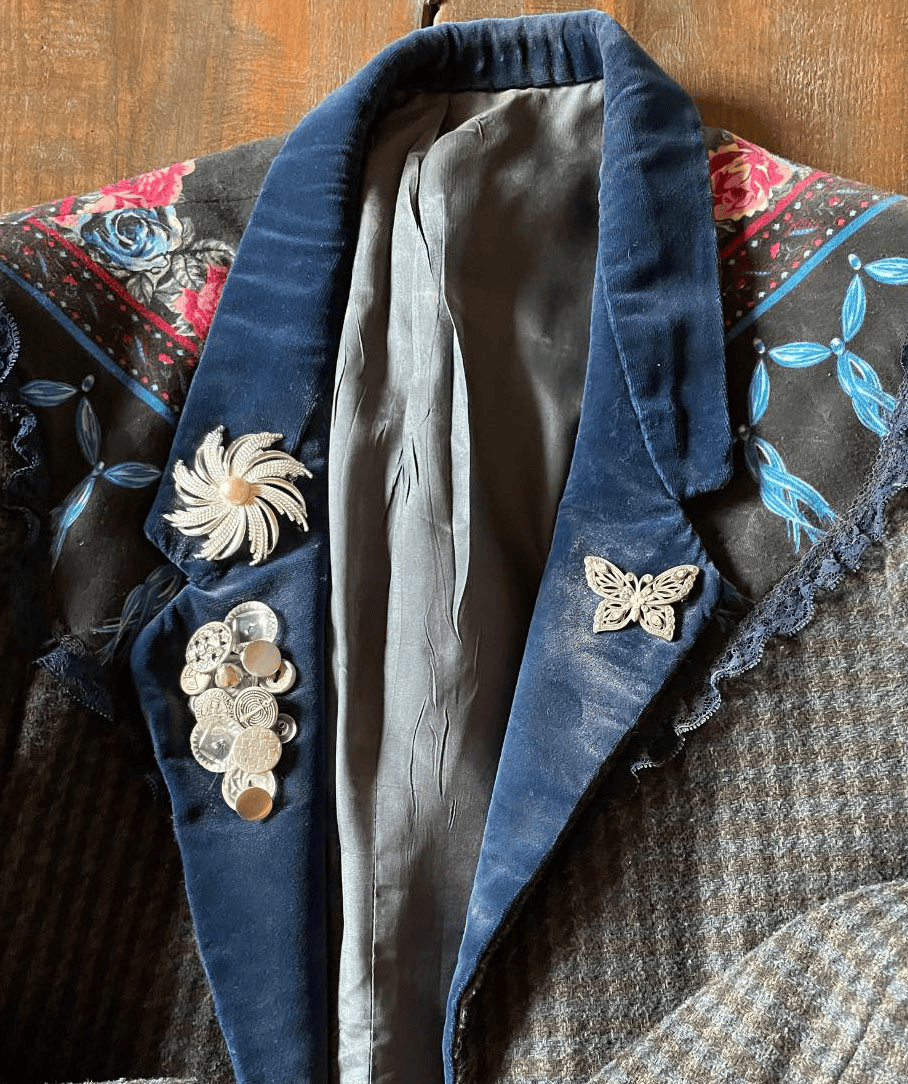 Dusty custom-decorated tweed blazer with velvet lapels, silver buttons, and lace trim on a wooden table