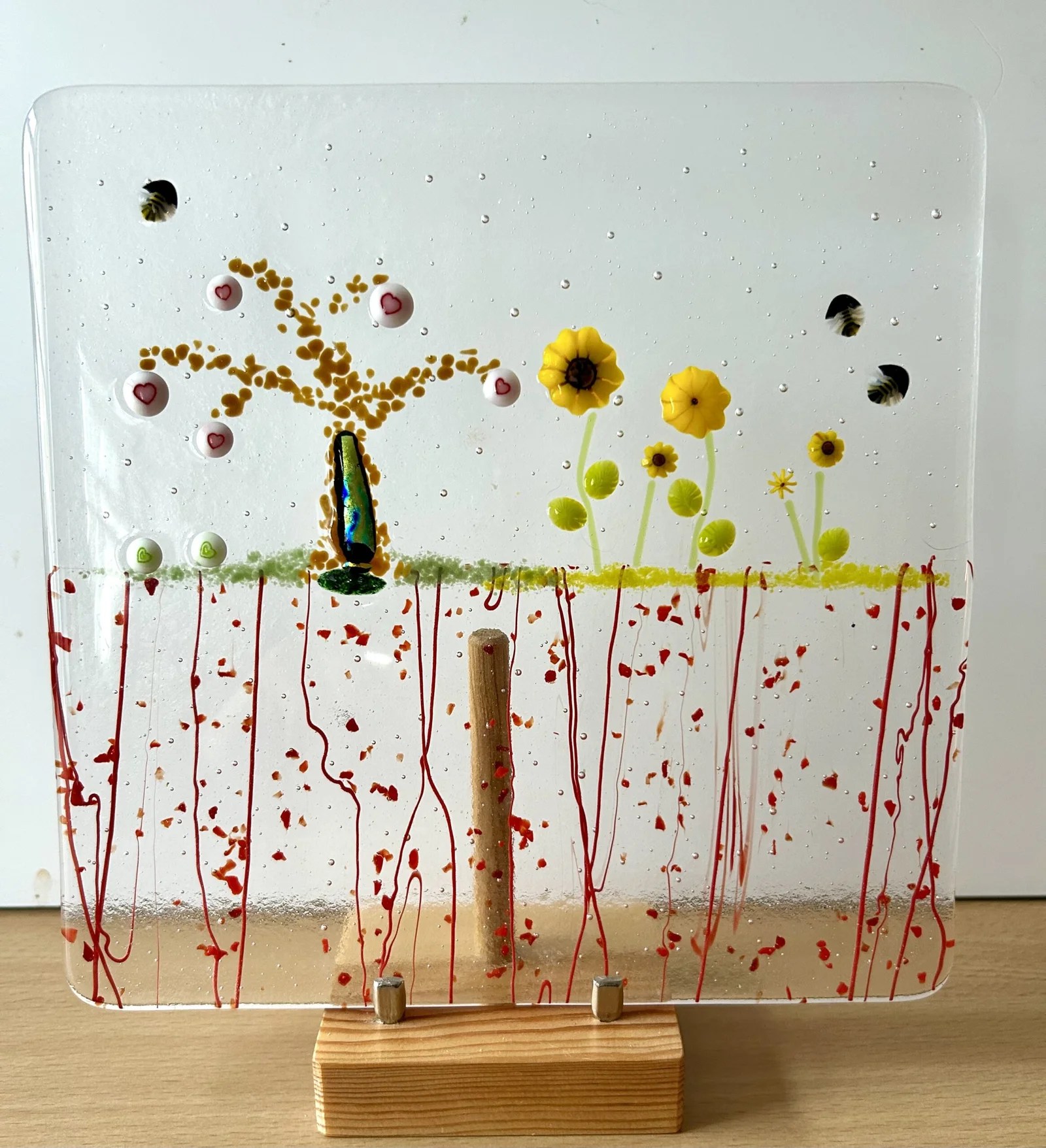 a fused glass picture with a tree, flowers, hearts and bees
