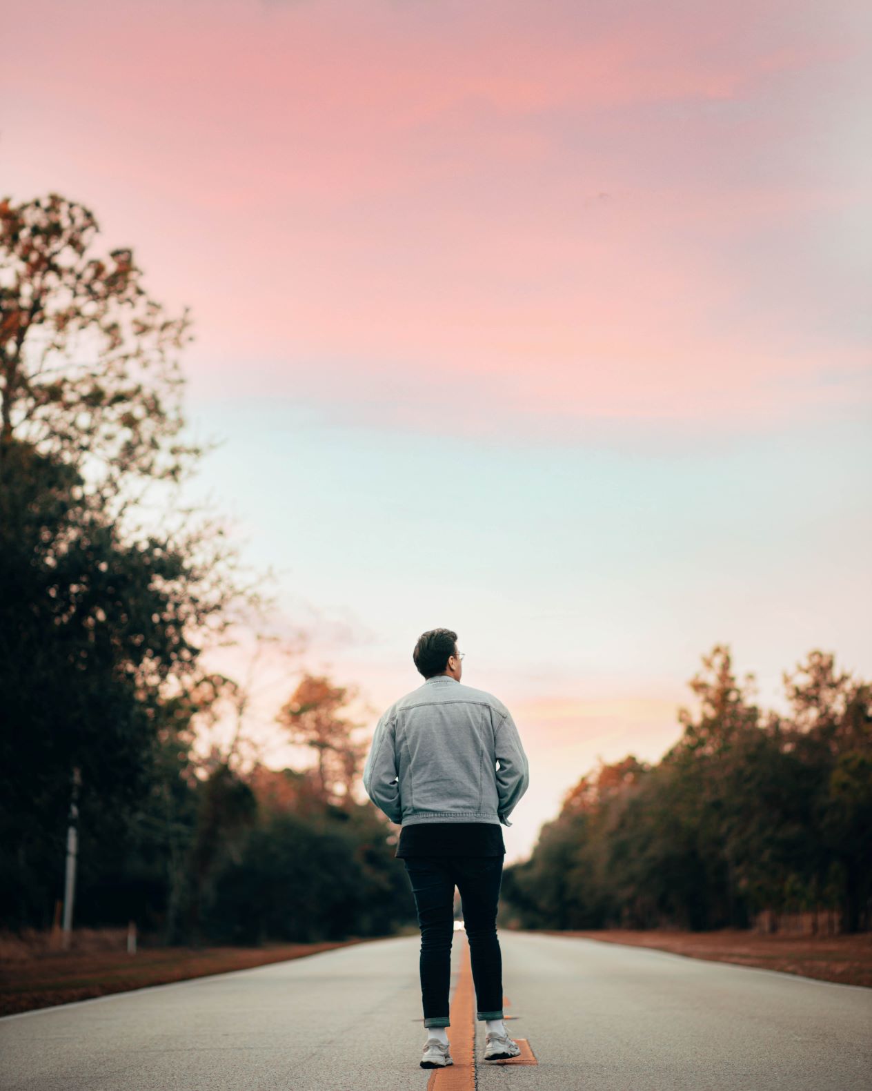 the back on a person standing on a road looking at a pink sky