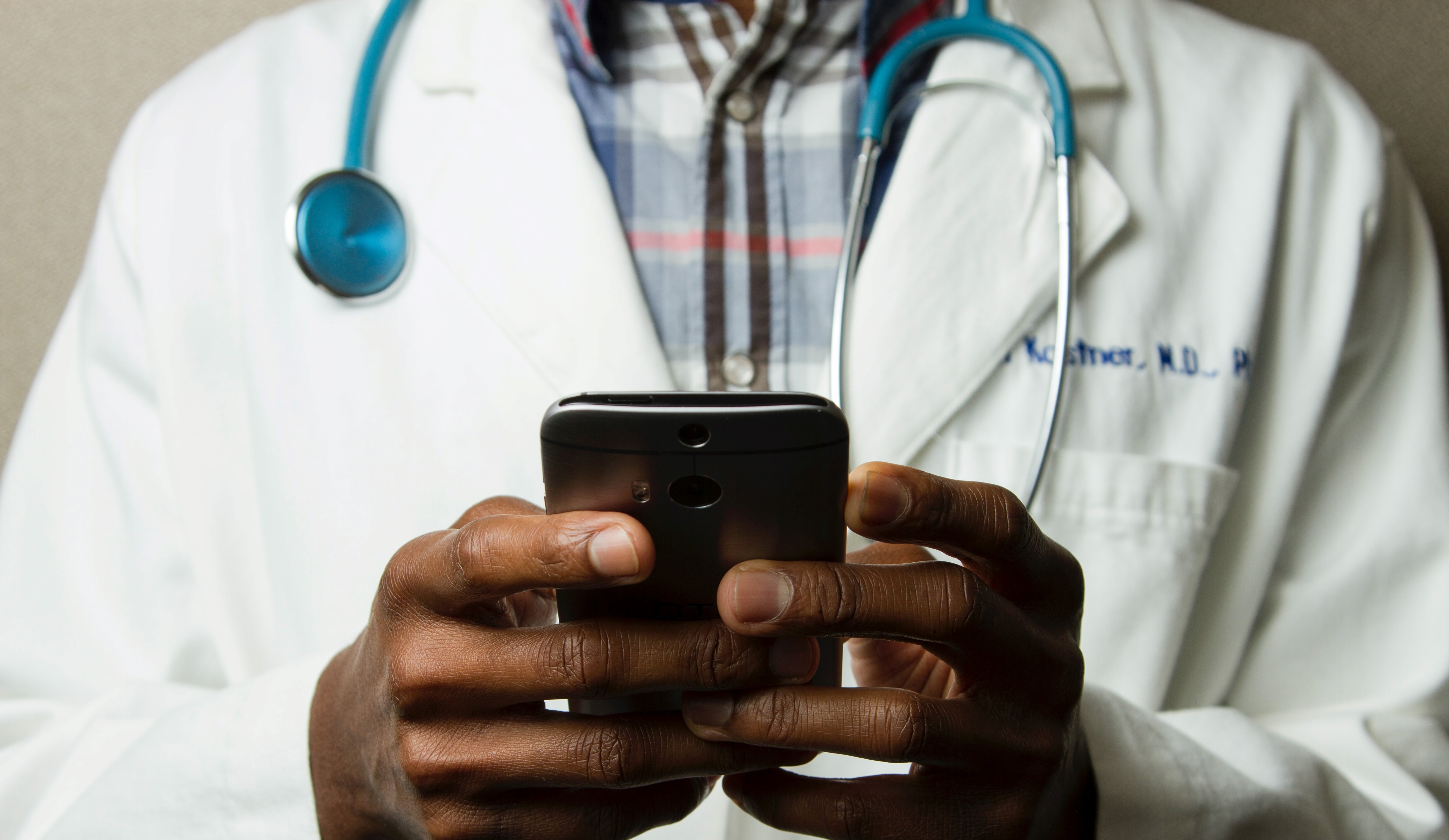 Image of person with white coat and stethoscope holding a phone