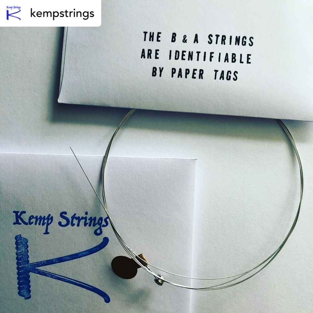 A photograph of Kemp Strings paper envelopes and a guitar string showing how the B and A strings are identifiable by paper tags.