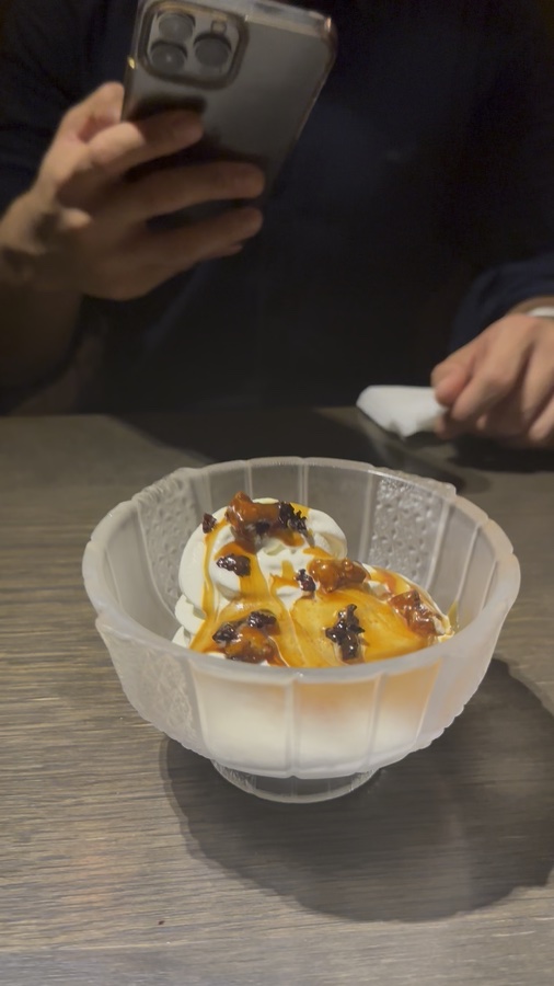 Ice cream with amber-colored sauce and toppings in a glass dish