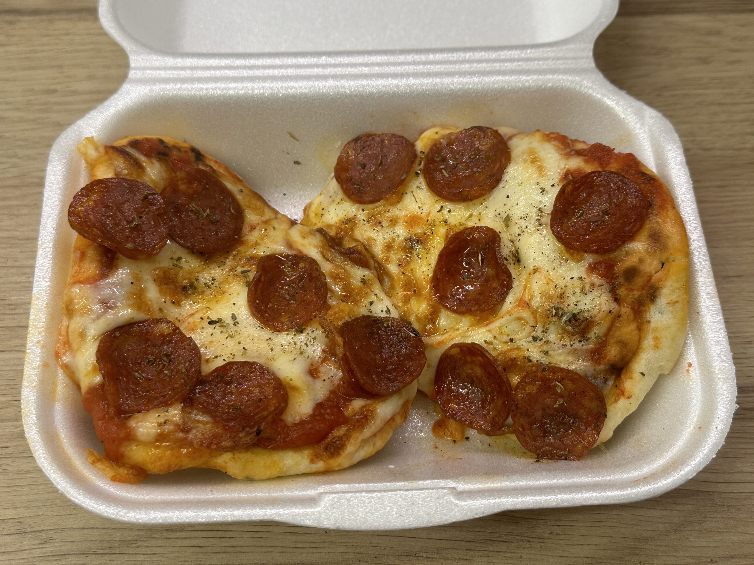 Naan pizza topped with pepperoni in a takeaway style container.