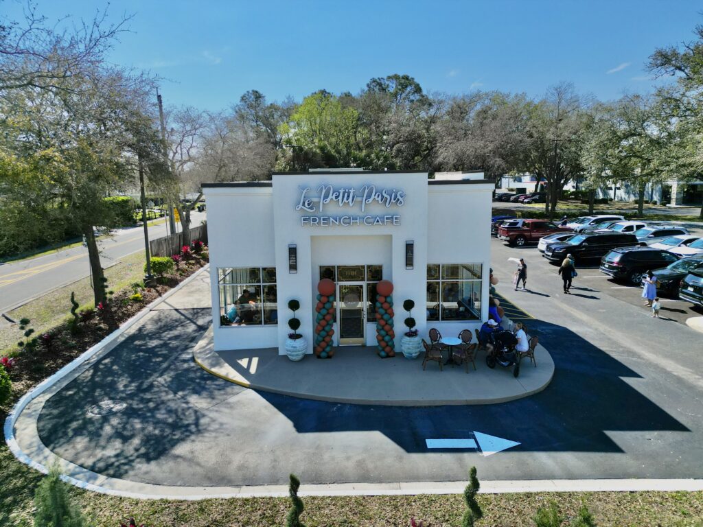 Aerial view of Le Petit Paris French Café’s grand opening, showcasing the café’s exterior with festive decorations and outdoor seating.