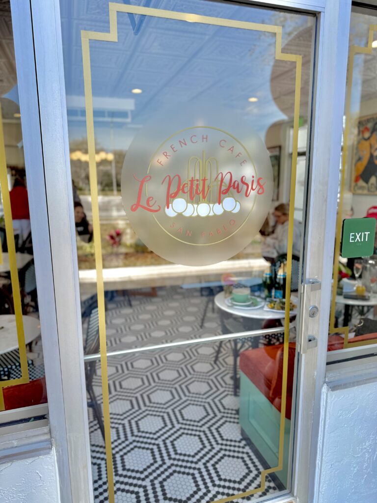 Close-up of the custom vinyl door decal at Le Petit Paris French Café, featuring an elegant gold-accented logo.