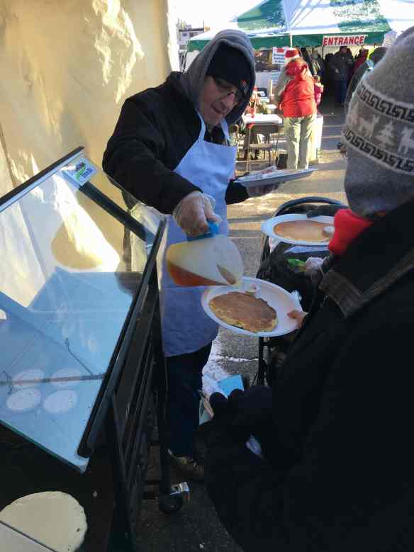 Man pours maple syrup onto a plate containing a pancake at the Elmira Maple Syrup Festival 