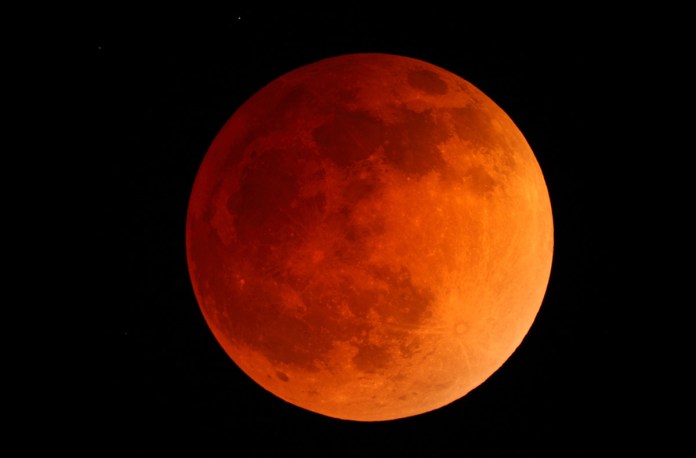 a red moon is seen in the dark sky