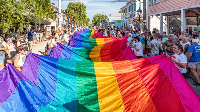 a group of people walking down a street holding a rainbow colored kite