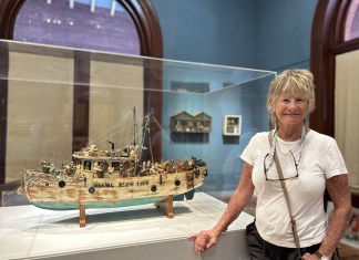 SHUTTER STORIES: ELIZABETH DEVRIES TURNS OLD WOODEN PANELS INTO ART a woman standing next to a model of a boat