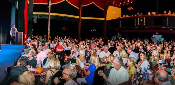 ddd a large group of people sitting at tables in front of a stage
