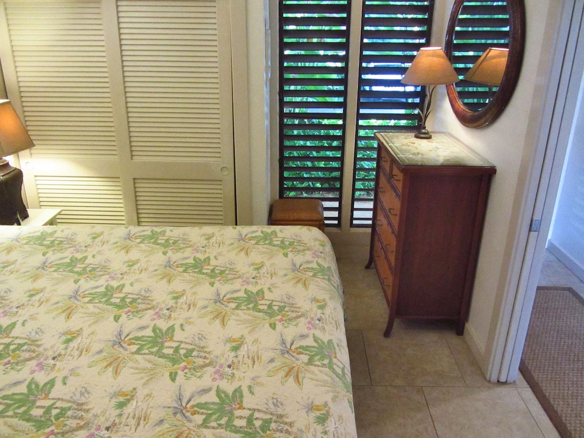 Picture of the bedroom showing part of the bed, the nightstand's lamp, the closet, the dresser, and the louvered full length windows.