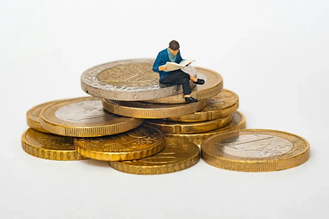 Miniature figure reading on stacked coins representing financial growth.