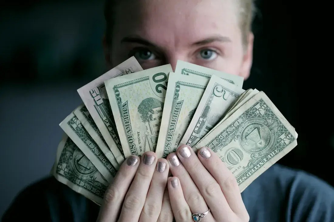 Person holding fan of U.S. dollar bills symbolising financial wealth and budgeting.