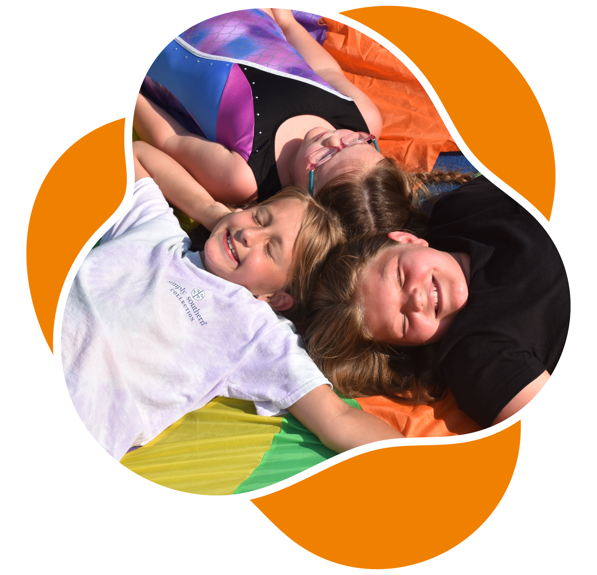 Three girls laying down on parachute, smiling with their eyes closed in the sunshine.