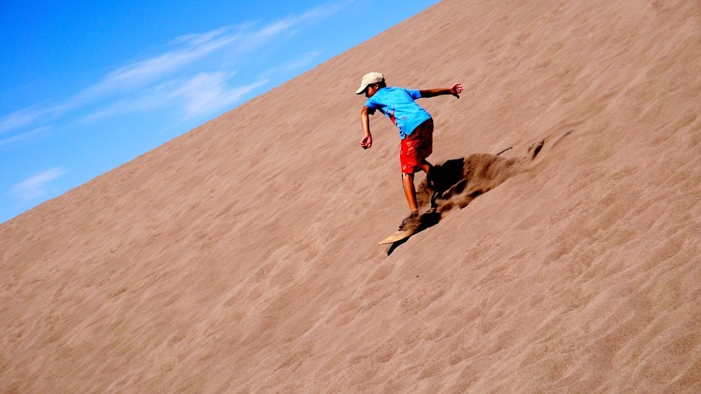Boy sliding down sand hill