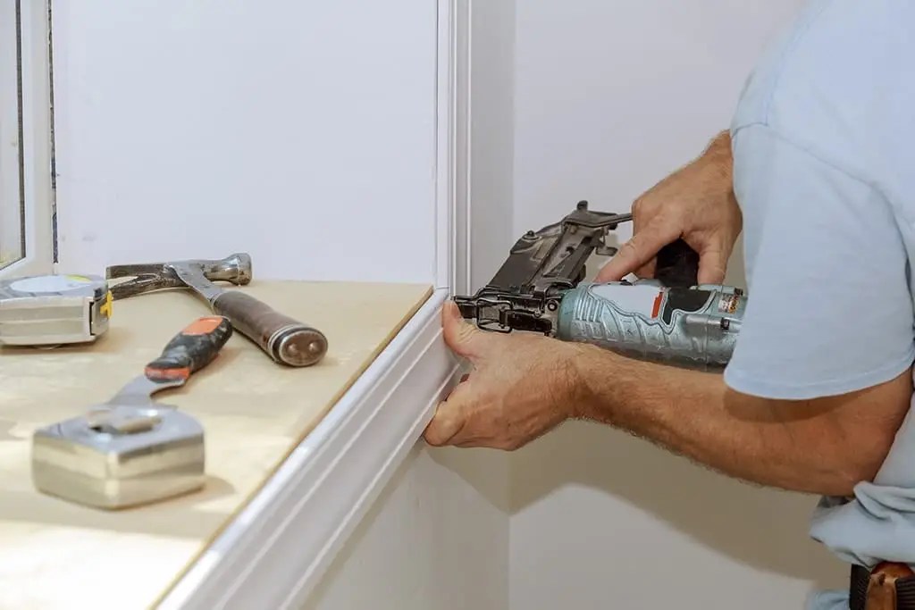 Person carefully installing wooden trim carpentry with precision tools, showcasing smooth edges and a clean finish.