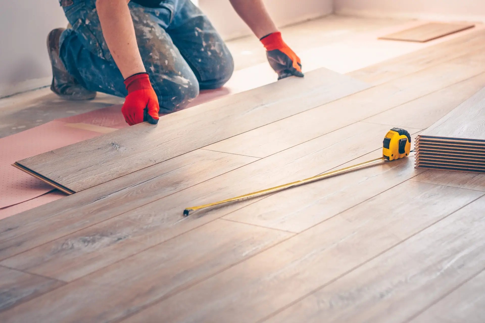 Worker kneeling and installing wood flooring panels with precision using professional tools.