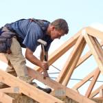 Skilled carpenter framing a house with wooden beams under clear sky during residential construction.