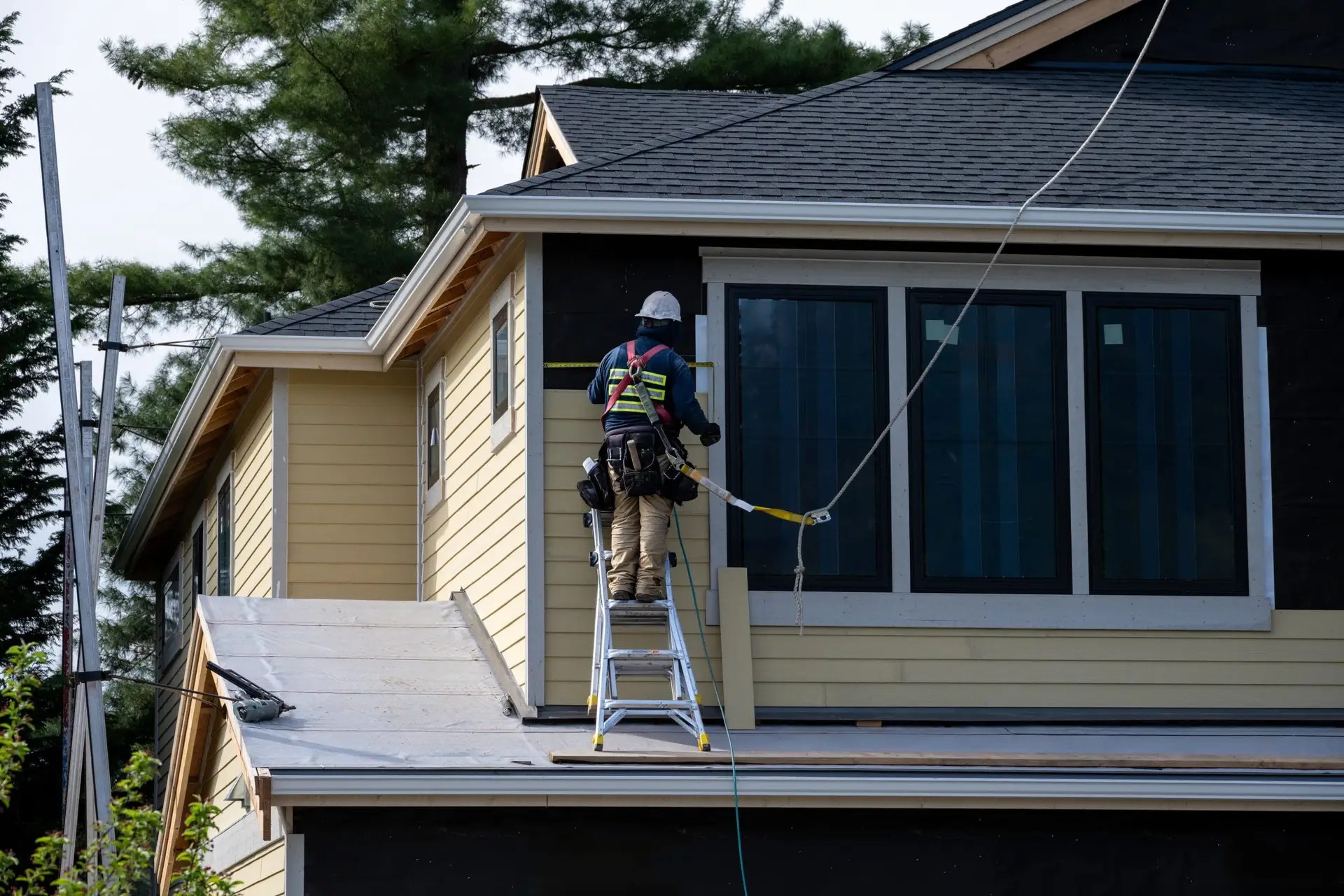Contractor installing vinyl siding panels on house exterior with tools and ladder, illustrating home siding process