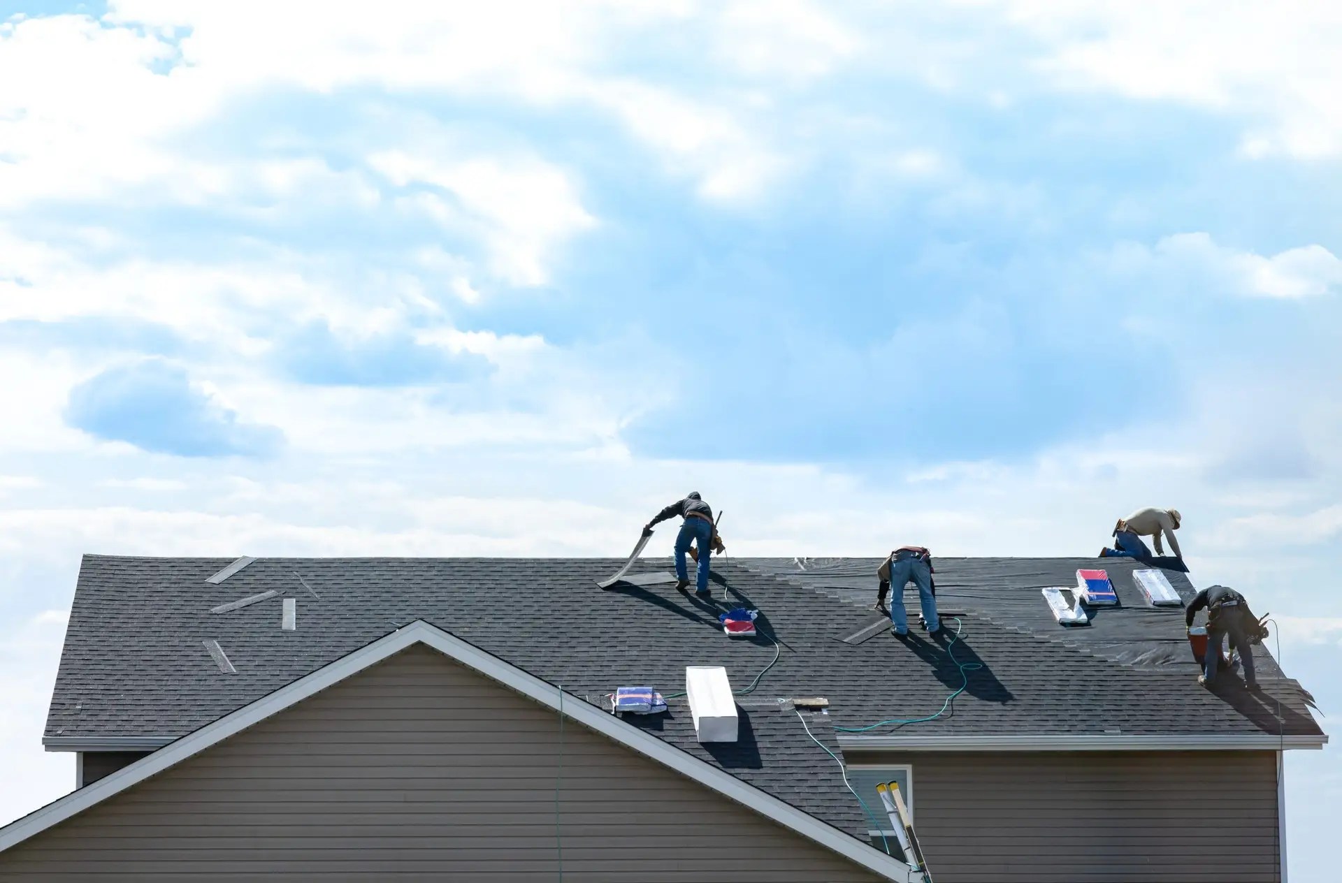 Roofer installing asphalt shingles on residential house roof, using tools and safety gear during home roofing construction