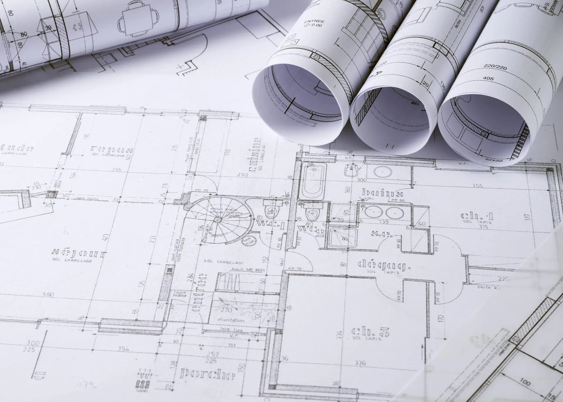 Rolled architectural building plans for a new house resting on wooden desk, detailed blueprints tied and ready for work