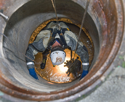 Employees inspect pipes through a maintenace hole