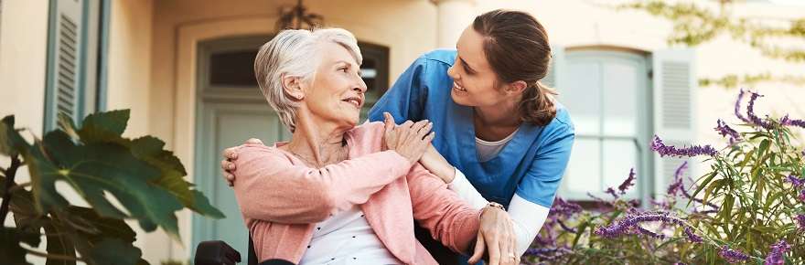 Healthcare support worker with an elderly woman in a wheelchair, talking outside nursing home.