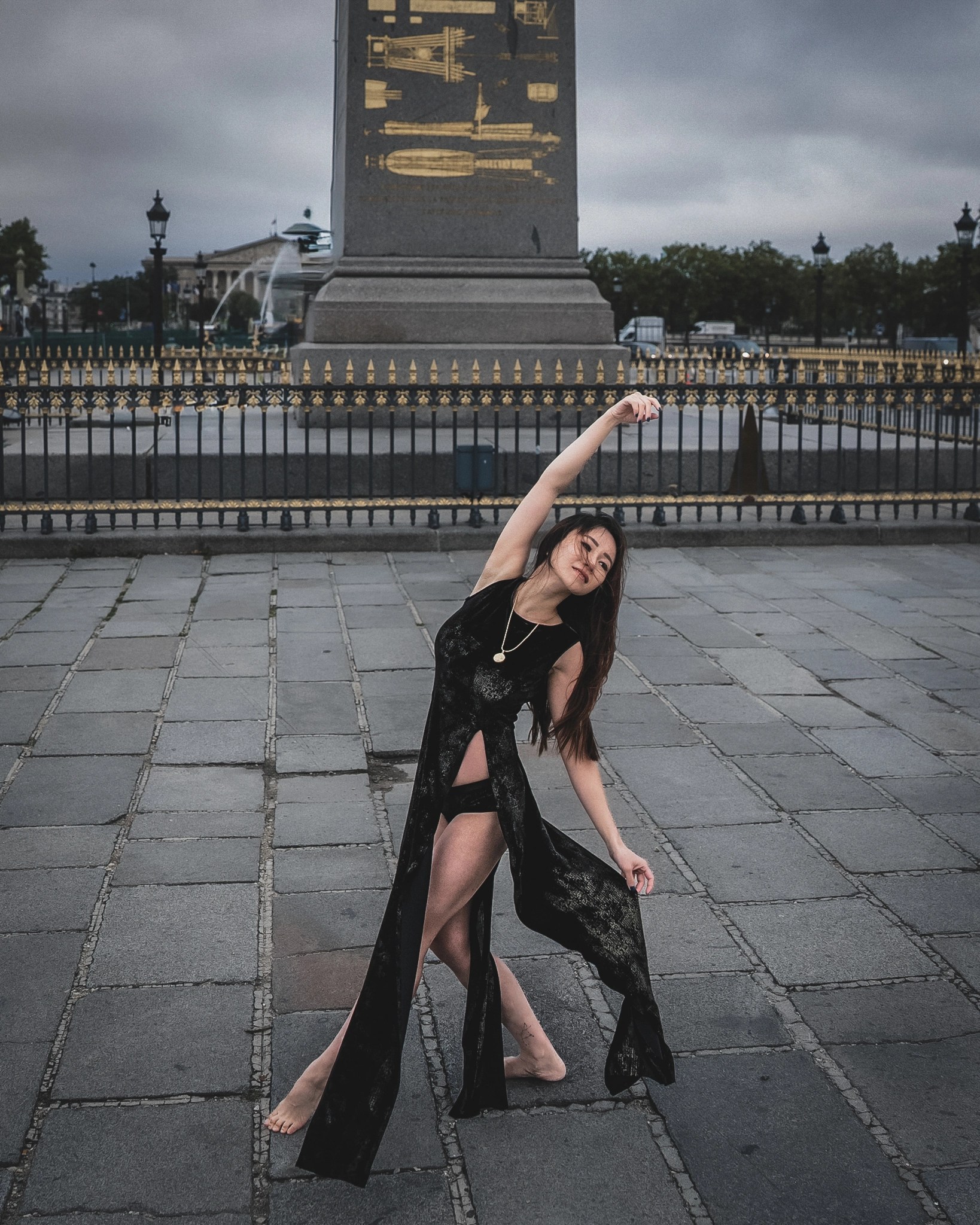 Lily Stadil bends sideways beneath the Luxor Obelisk at Place de la Concorde