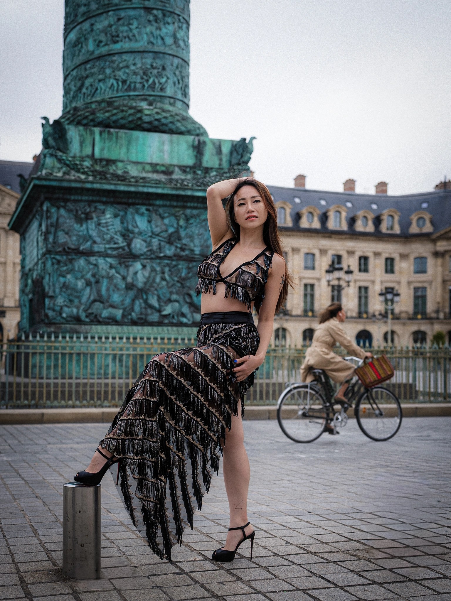 Lily Stadil poses by the Vendôme Column as a cyclist passes behind her